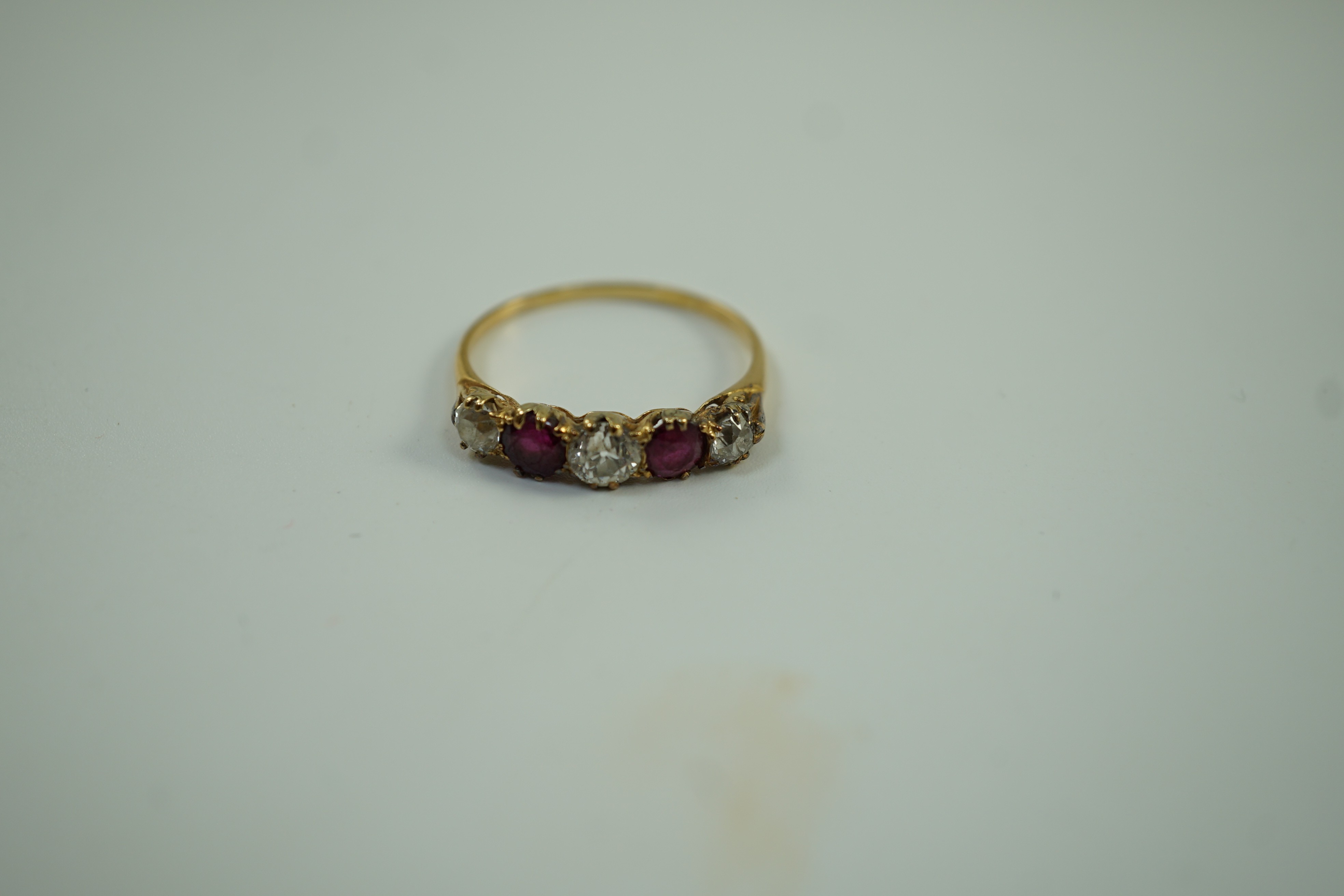 A yellow metal, three stone diamond and two stone ruby set half hoop ring, size V, gross weight 3.2 grams.
